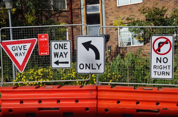 Sydney, New South Wales, Australia - August 5, 2018: Signs on a construction barrier fence next to inner-city road work advise motorists to Give Way, No Stopping, One Way, left-turn only and No Right Turn.