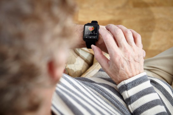 Senior man sitting in armchair using smartwatch