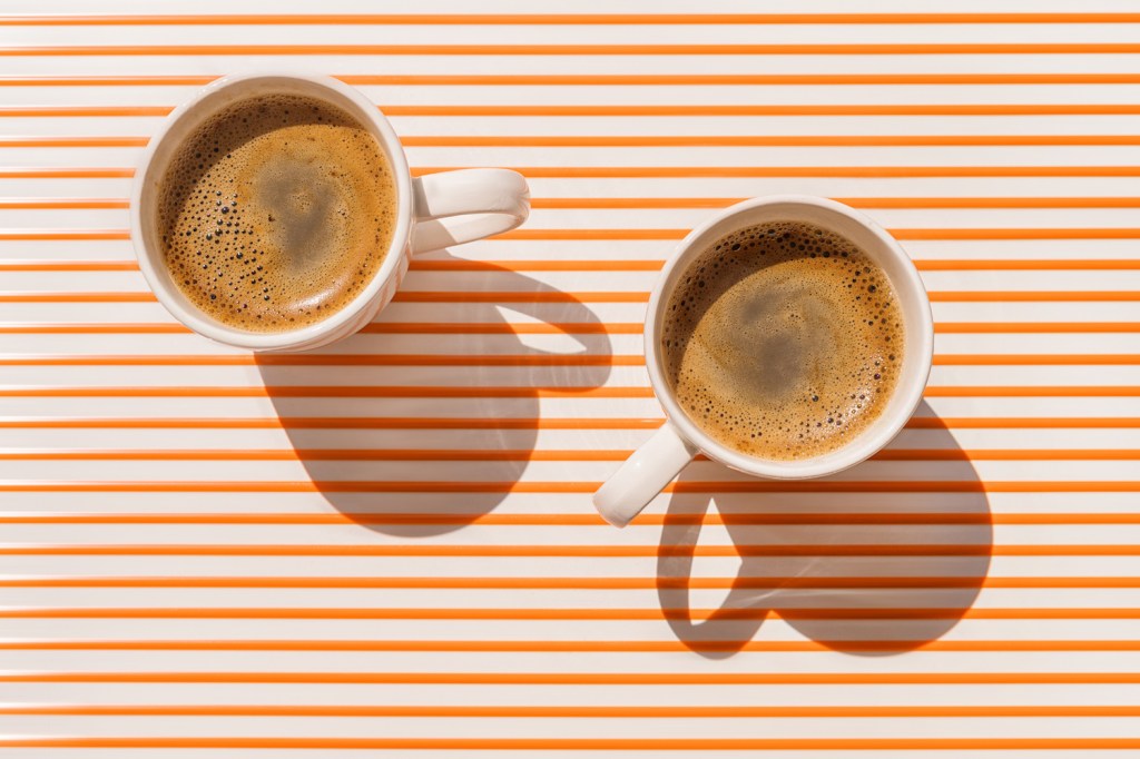 Two white coffee cup on orange striped table at direct sunlight. Top view with shadow.