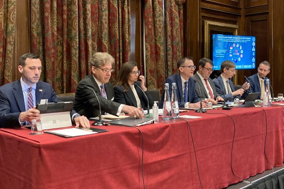 a photo of UK and US officials sitting at a red table discussing the LockBit takedown
