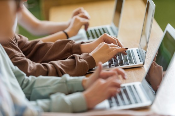 High school students sitting at the desk in the classroom during lesson, using laptops. Close up of hands, unrecognizable people.