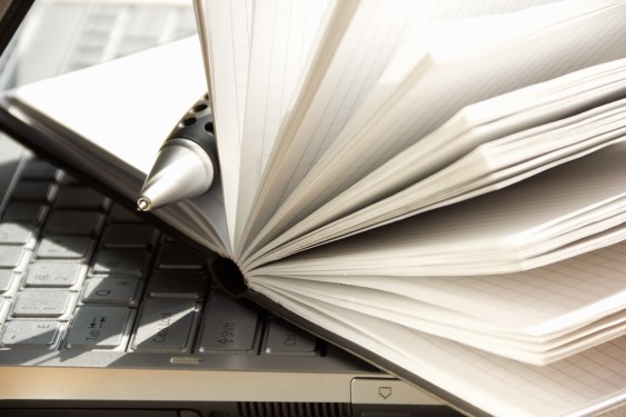 Notebook with pen sticking out, sitting on top of a laptop computer.