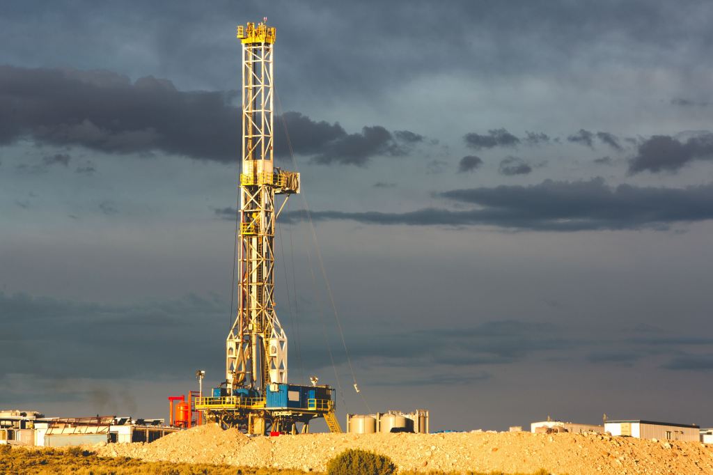 A rig drills into the earth against a cloudy sky.