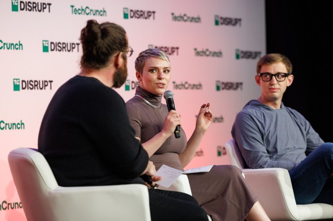 a photo of Zack Whittaker on stage with Heather Gantt-Evans, holding a microphone, and Darren Gruber.