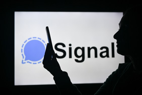 silhouette of person looking at phone in front of Signal logo