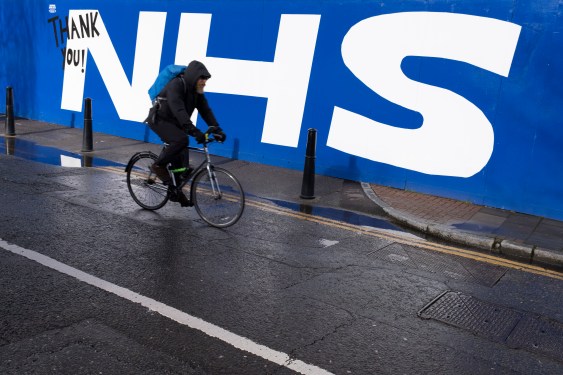 bike rider passes 'NHS' in large white letters on blue wall