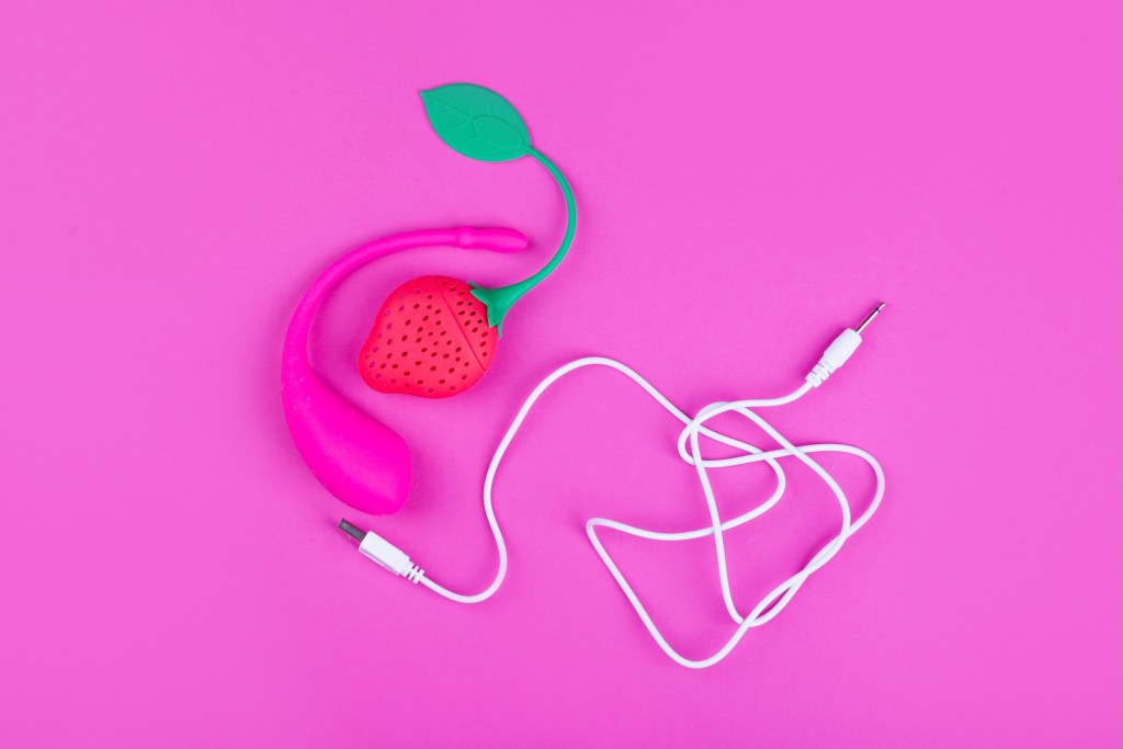 a photo of a female sex toy on a pink background, with a USB cable in the same shot