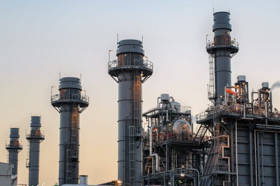 Natural gas power plant smoke stacks stand against a twilight sky.