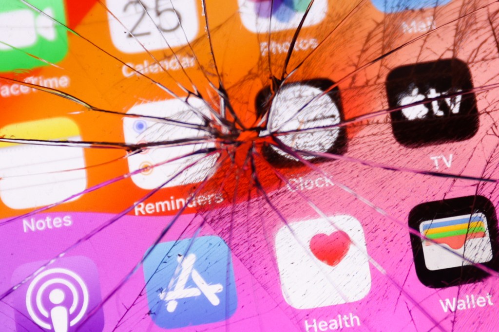 App icons displayed on a phone screen are seen through the broken glass in this illustration photo.