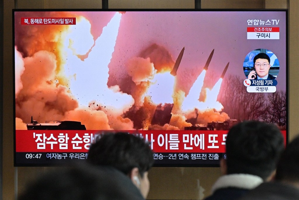 People stand near a television showing a news broadcast with file footage of a North Korean missile test, at a railway station in Seoul on March 14, 2023. - North Korea fired two short-range ballistic missiles on March 14, 2023, Seoul said, Pyongyang's second launch in three days and the first since South Korea and the United States began their largest joint military drills in five years.