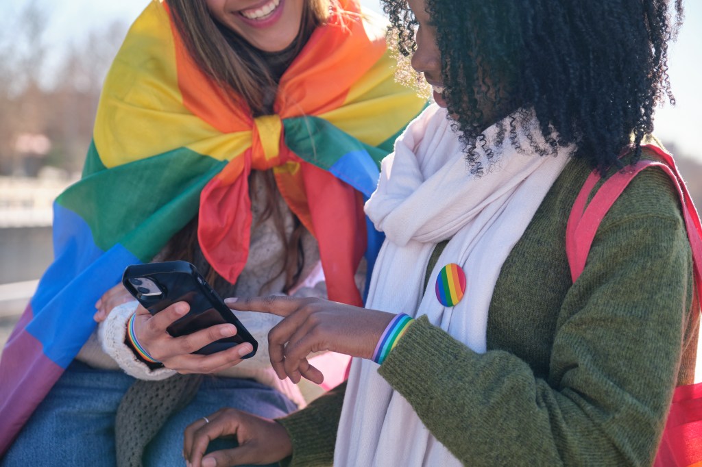 Two young women are using a smartphone while showing their support for LGBTQ+ rights