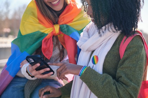 Two young women are using a smartphone while showing their support for LGBTQ+ rights