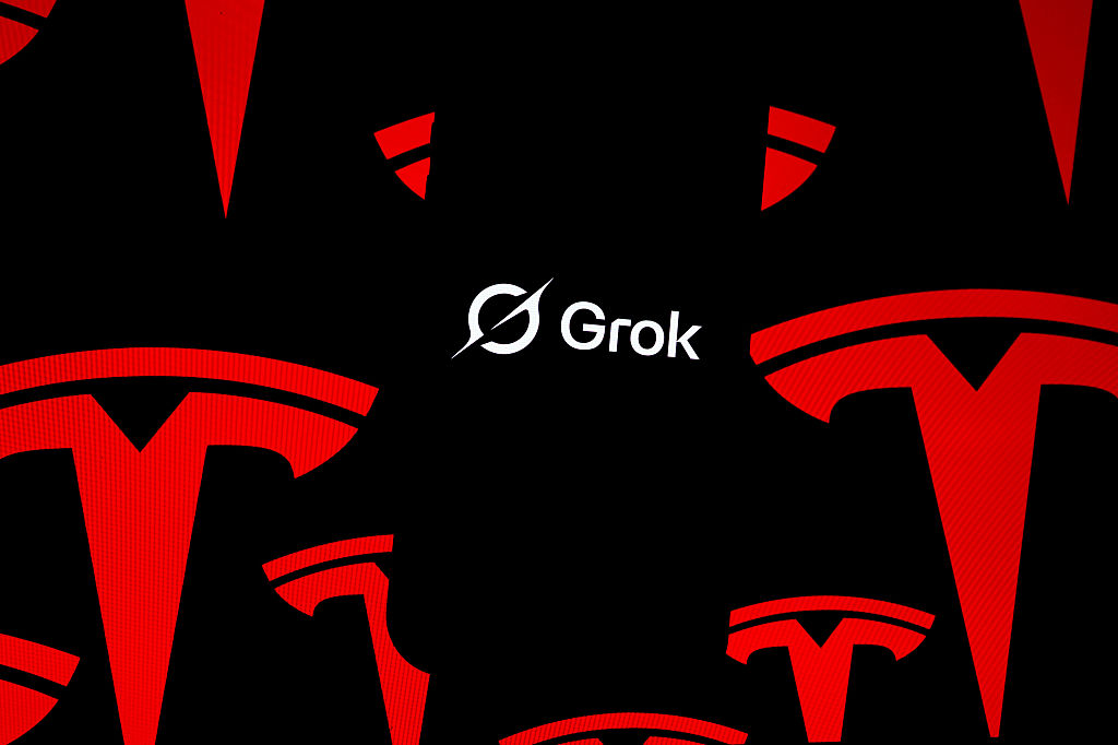 In this photo illustration, 'Grok' logo is seen displayed on a mobile phone screen in front of 'Tesla' logos.