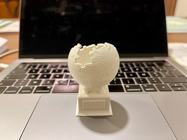 A 3D-printed version of the Wikipedia logo rests on the touchpad of an open MacBook.