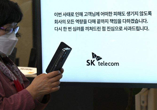 A woman uses her mobile phone while waiting to replace her USIM ship in front of an SK Telecom branch in Seoul on April 28, 2025.