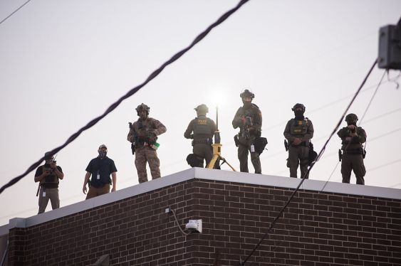 U.S. Immigration and Customs Enforcement (ICE) agents, Department of Homeland Security (DHS) personnel, and Border Patrol Commander Gregory Bovino stand together amidst a tense protest outside the ICE processing facility in Broadview, Illinois, on September 27, 2025.